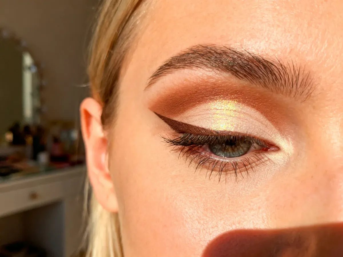 Zbliżenie na oko z precyzyjnym makijażem typu cut crease, łączącym matowy brąz z połyskującym cieniem na powiece.